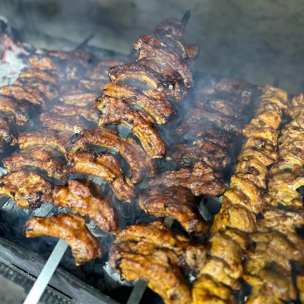 Skewers of marinated lamb ribs and chicken cooking over smoky charcoal at Tonir Cafe.