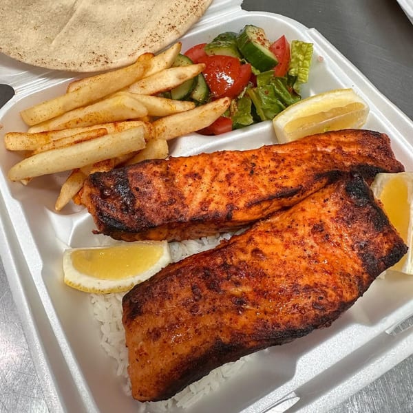 Two grilled salmon fillets with rice, fries, salad, lemon wedges, and pita bread in a takeout container.