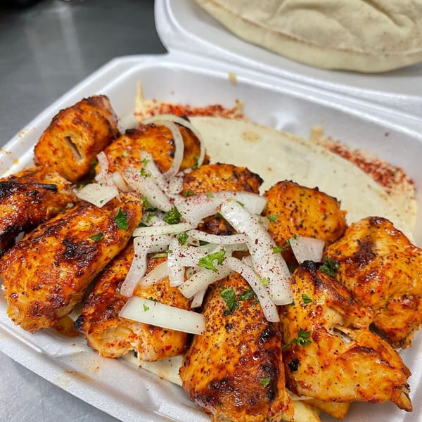 Grilled chicken shish tawook with sliced onions, parsley, and sumac, served in a takeout container.